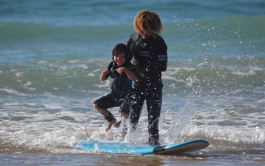 Le coach accompagne un jeune surfeur dans la mousse